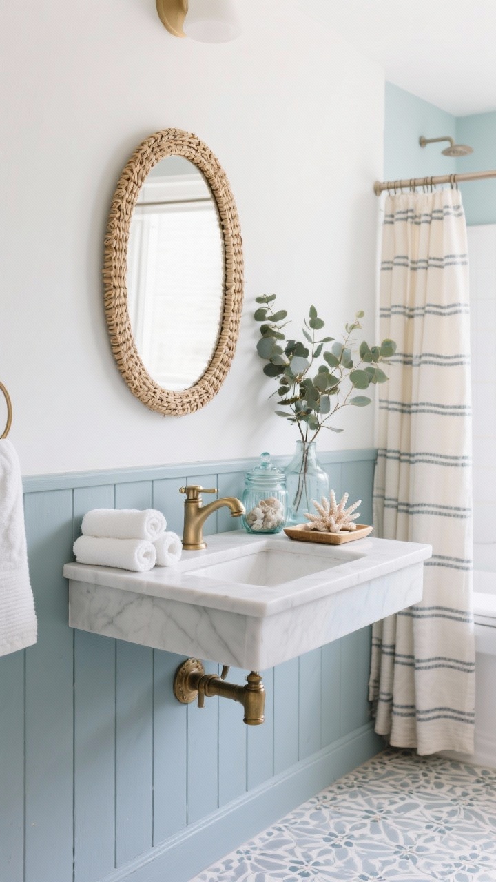 Detail-oriented medium shot of a coastal modern bathroom vanity wall: lower half in board-and-batten painted misty blue-gray, upper half limewashed in pearly sea-salt white; arched rattan-framed mirror above a simple vanity with brushed nickel (or unlacquered brass) faucet and hardware; vanity styled with rolled white towels, sea glass jars, and a small tray holding coral-inspired soap dishes; glimpse of patterned porcelain or faux-zellige floor; waffle shower curtain and striped Turkish towels in the background; eucalyptus bundle adding freshness; palette of mist blue, sea salt white, sandy beige, brass/nickel; airy, spa-like, photorealistic.